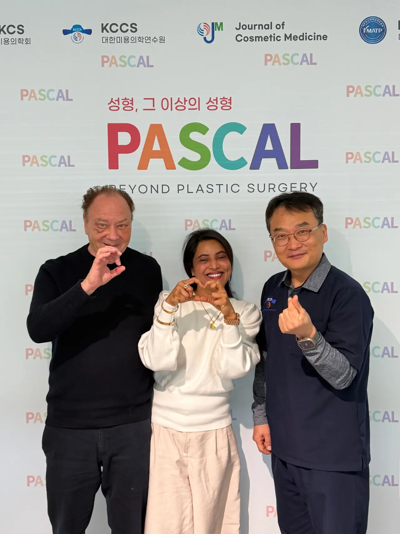 Two visiting doctors with a Pascal doctor in front of the Pascal Beyond Plastic Surgery backdrop